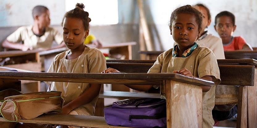 Klasserom med unge elever fra Madagaskar. To jenter sitter ved en pult nærmest fotografen og den ene ser mot fotografen.